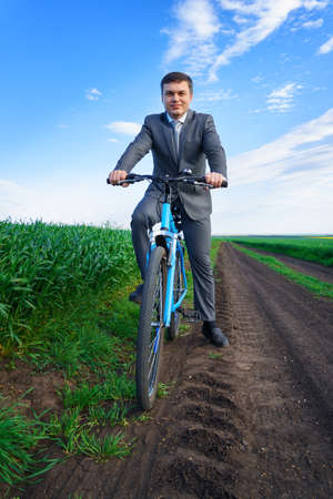 Businessman with a bicycle posing in a green grass field - business concept for freedom, vacation or freelance. Beautiful spring nature.の写真素材