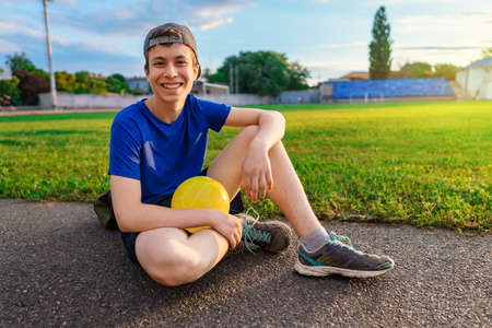 concept of sports and health - portrait of a teen boy posing at a stadium track, a soccer field with green grassの写真素材
