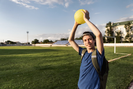 concept of sports and health - portrait of a teen boy posing at a stadium track, a soccer field with green grassの写真素材