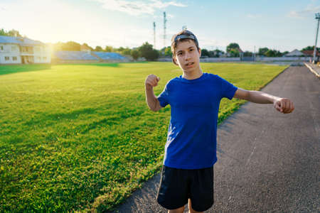 concept of sports and health - portrait of a teen boy posing at a stadium track, a soccer field with green grassの写真素材