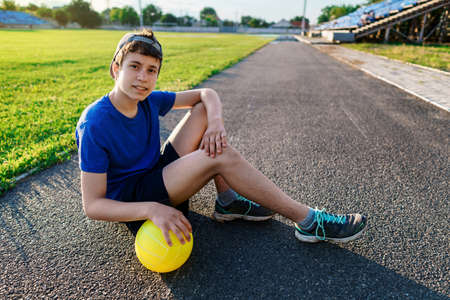 concept of sports and health - portrait of a teen boy posing at a stadium track, a soccer field with green grassの写真素材