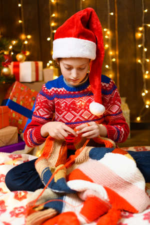 Child girl posing in new year or christmas decoration. Festive lights and lots of gifts, an elegant Christmas tree with toys. The girl is wearing a red sweater and a Santa hat, she plaing with bearの写真素材