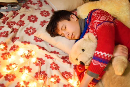 Boy sleeping in new year or christmas decoration. Holiday lights, gifts and christmas tree decorated...
