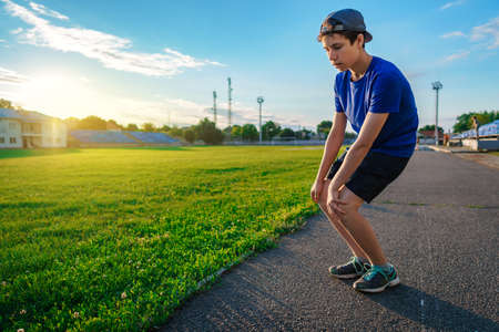 happy teen boy portrait at a sport stadium, he's wearing headphones and smiling, a soccer field with green grass - sports and health conceptの写真素材