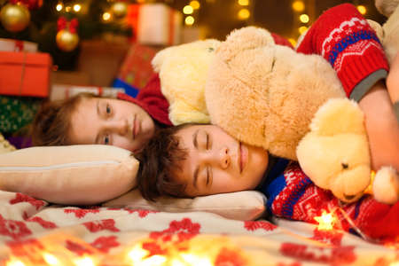 Children sleeping in new year or christmas decoration. Teenage boy and girl. Holiday lights, gifts and christmas tree decorated with toys.の写真素材