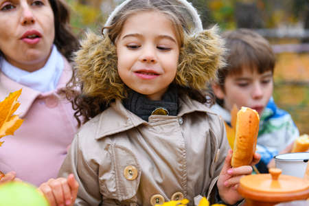 Portrait of a happy family in an autumn park. People are sitting at the table, eating and talking. Posing against the background of beautiful yellow trees. They are happy together.の写真素材