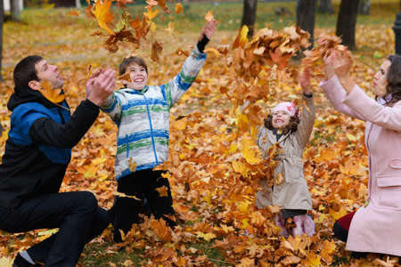 Happy family resting in autumn city park. People are sitting at the table, eating and talking. Posing against the background of beautiful yellow trees. They are happy together.の写真素材
