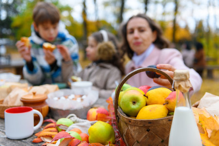 Portrait of a girl eating a bun. Happy family resting in autumn city park. People are sitting at the table, eating and talking. Posing against the background of beautiful yellow trees.の写真素材