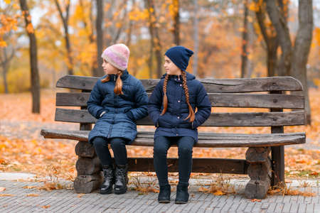 portrait of a children in an autumn city park - happy people sitting together on a wooden bench, posing against a background of beautiful yellow leavesの写真素材