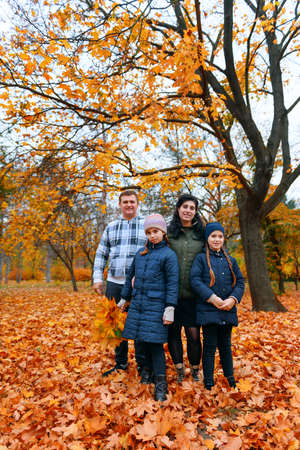 Portrait of a family with children in an autumn city park - happy people posing together near big tree, beautiful nature with yellow leaves as background.の写真素材