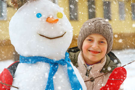 a girl plays with snow on a city street and makes a snowmanの写真素材