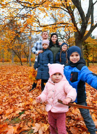 Portrait of a family with children in an autumn city park - happy people posing together near big tree, beautiful nature with yellow leaves as background.の写真素材