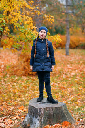 Portrait of a child girl in autumn city park. Posing with maple leaf. Beautiful nature, trees with yellow leaves.の写真素材
