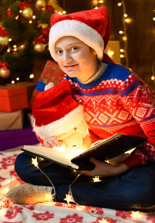 Child girl as Santa helper posing in new year decoration. Wearing a protective face mask against viruses, coronaviruses. She plays with a toy bear, cures him and gives him pills.の写真素材