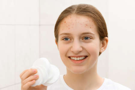 girl puts cream on her face, face of a teenage girl with good skin, she looks at herself in the mirror, concept of beauty and healthの写真素材