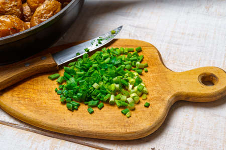chopped green onions and fried potatoes in a frying pan, cooked food in a rustic style on a background of white wooden boardsの写真素材