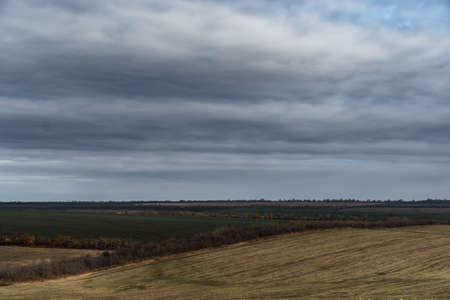 dramatic landscape, late autumn, agricultural field with dry wheat and wild grass, cloudy weather with a stormy skyの写真素材
