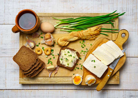 tasty lunch in rural style, healthy food - glass of beer, bread and butter sandwich, feta cheese, eggs, green leek and rye bread, cooked food on a white wooden boardsの写真素材