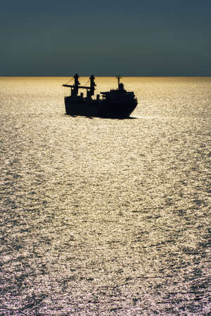 silhouettes of ship at sea, dramatic seascape with sunset sky, bright sunlight reflected from the wavesの写真素材