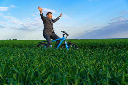 business concept - A businessman poses with bicycle on a green grass field, dressed in a business suit, he looking for something in a briefcaseの写真素材