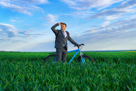 businessman poses with backpack and bicycle in a green grass field, dressed in a business suit, beautiful nature in spring, business conceptの写真素材