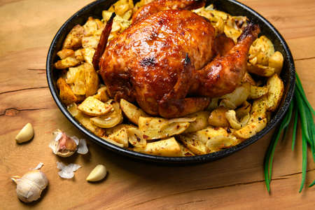 roasted potatoes and baked chicken meat in a frying pan, cooked food, delicious crust, one object on a wooden backgroundの写真素材