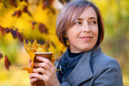 beautiful woman with autumn yellow leaves takes a selfie on her phone, posing in a city park, bright sunny day in fall seasonの写真素材