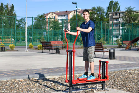 a teenage boy trains on a sports ground outdoors, he does physical exercises, a healthy lifestyle, a bright sunny day in summerの写真素材
