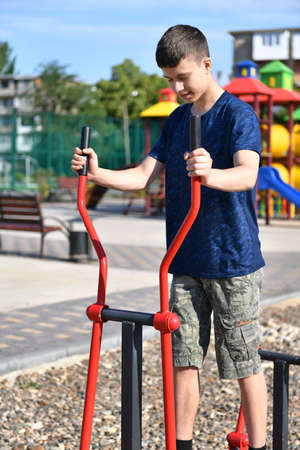 a teenage boy trains on a sports ground outdoors, he does physical exercises, a healthy lifestyle, a bright sunny day in summerの写真素材