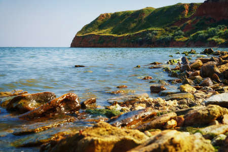 beautiful summer seascape, seashore on a bright day, high hill, wild grass and stonesの写真素材