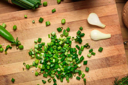 vegetables on a wooden kitchen board, sliced green onions, peas on a wood background, concept of fresh and healthy food, still lifeの写真素材