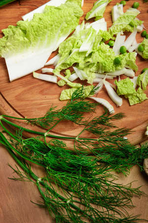vegetables on a wooden kitchen board, green onions, dill and peas, sliced cabbage on a wood...
