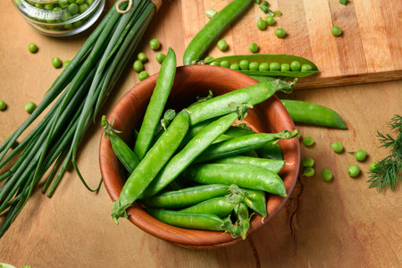 vegetables on a wooden kitchen board, sliced green onions, dill and peas on a wood background,...