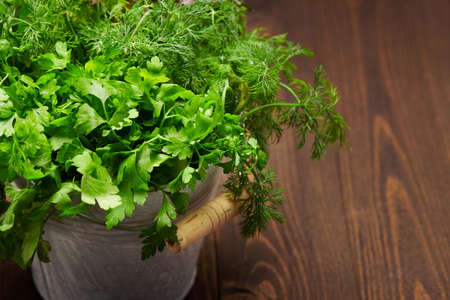a bunch of green dill, parsley, salad and other greens in an iron bucket, dark wooden background, concept of fresh vegetables and healthy foodの写真素材