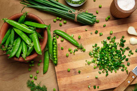 vegetables on a wooden kitchen board, sliced green onions, dill and peas on a wood background, concept of fresh and healthy food, still lifeの写真素材
