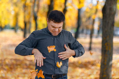 portrait of a disgruntled man, he poses with yellow leaves in an autumn park, his face has an unhappy grimace and lack of joy, a bright sunny dayの写真素材
