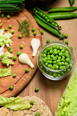 vegetables on a wooden kitchen board, green onions, dill and peas, sliced cabbage on a wood background, concept of fresh and healthy food, still lifeの写真素材