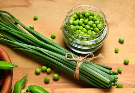 vegetables on a wooden kitchen board, sliced green onions, peas on a wood background, concept of fresh and healthy food, still lifeの写真素材
