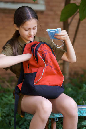 a teenage girl, being a student, sits on a bench near the school building, a girl takes a protective...