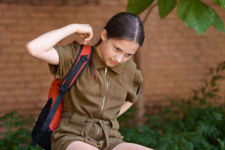 a teenage girl, being a student, sits on a bench near the school building, she puts on a backpackの写真素材