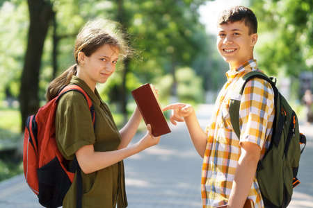 students a boy and a girl are sitting on a bench outside the school building, they are reading books