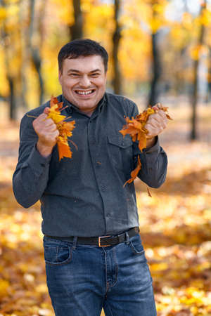 portrait of a disgruntled man, he tears yellow leaves in an autumn park, a disgruntled grimace and lack of joy on his face, a bright sunny dayの写真素材
