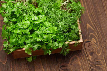 a top of bunch of green dill, parsley, salad, herbs and other greens in a wooden box, dark wood background, concept of fresh vegetables and healthy foodの写真素材
