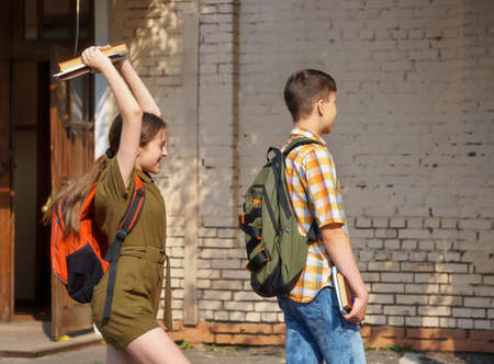 schoolchildren are having fun in the school yard - a teenage girl wants to hit a boy on the head with booksの写真素材
