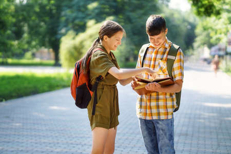 portrait of students in a city park, teenage schoolchildren a boy and a girl are standing on the path and discussing lessons, reading a book and talkingの写真素材