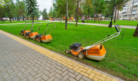 lawn mowers at the edge of the lawn in a city park, a path made of paving slabs, green grass and urban architectureの写真素材