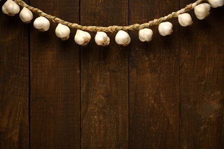 garlic bulbs braided in a pigtail like a garland on a background of dark wooden boards, an empty place for textの写真素材