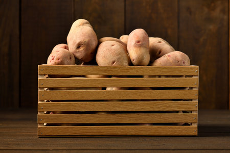 wooden box full of potatoes on dark wooden backgroundの写真素材