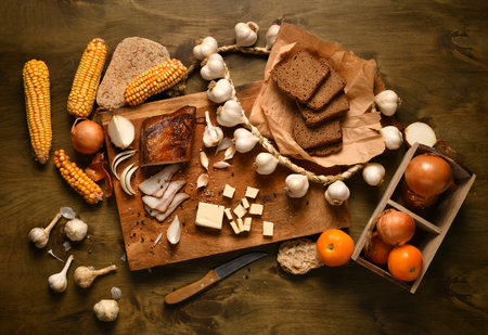 still life of food in a rural style on a dark wood background, lard and garlic, cheese, tomatoes and corn with rye bread, concept of fresh vegetables and healthy foodの写真素材