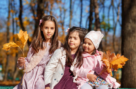 portrait of girls in an autumn city park, children sitting on a bench, talking and enjoying the...